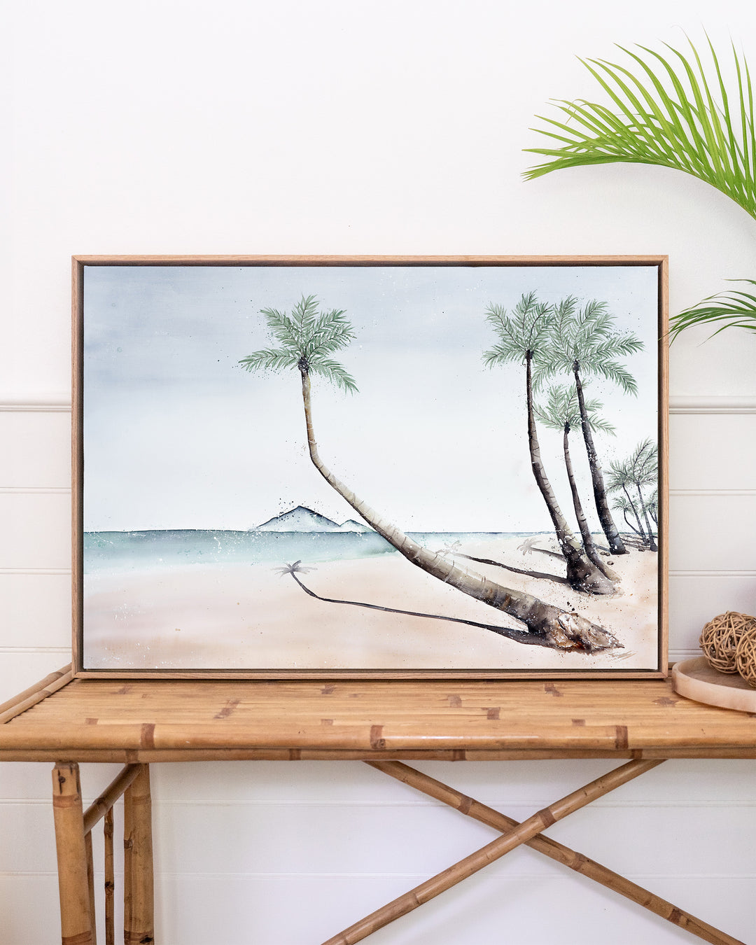 Where The Palm Trees Lead – Port Douglas beach and palm trees, framed canvas in oak float frame, styled on a rattan table