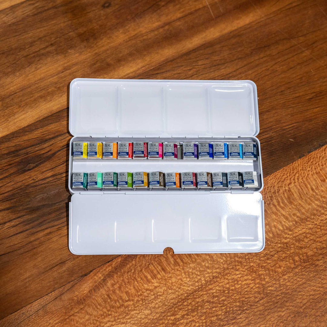 Windsor &amp; Newton 24 Piece Watercolour Set with bright pigments in a white metal case, displayed on a wooden surface.