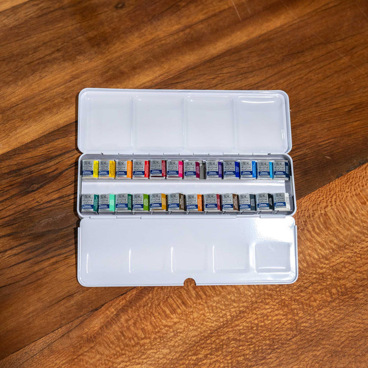 Windsor &amp; Newton 24 Piece Watercolour Set with bright pigments in a white metal case, displayed on a wooden surface.