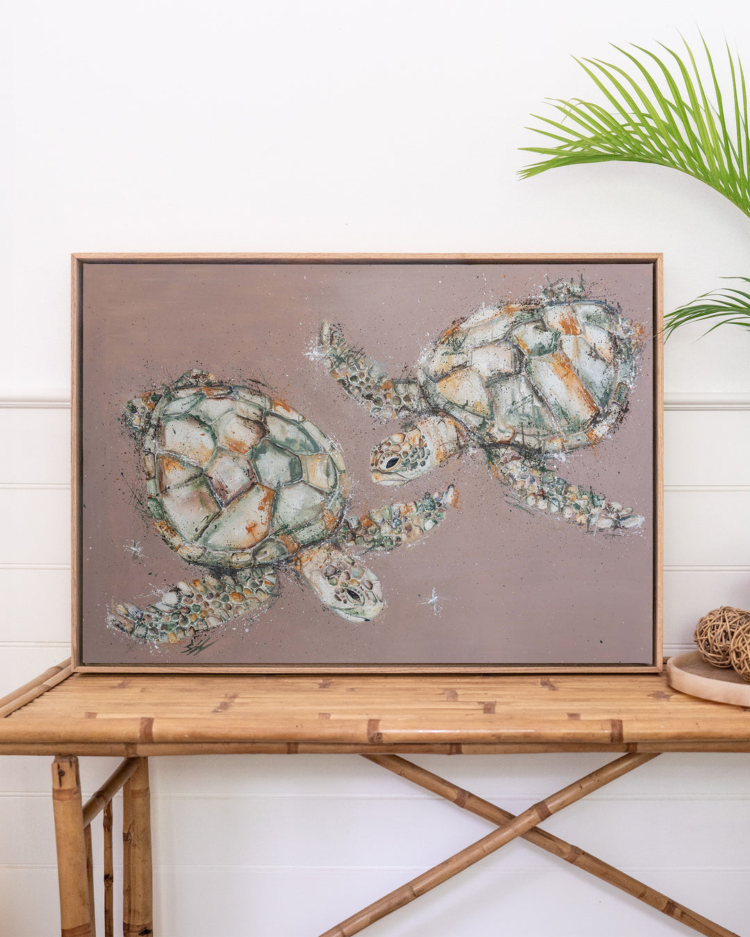 Winter Solstice – green sea turtles, framed canvas in oak float frame, styled on a rattan table